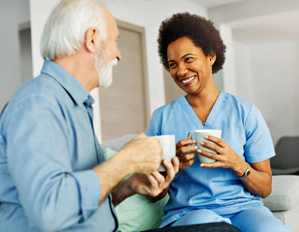 Doctor Or Nurse Caregiver With Senior Man Drinking Tea Or Coffee